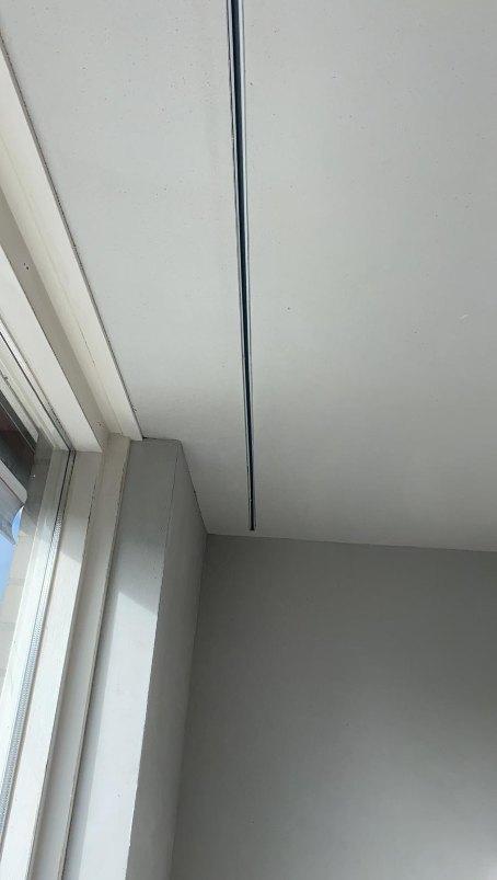 Strakke sleuf in het gestucte plafond waar de gordijnrails is weggewerkt