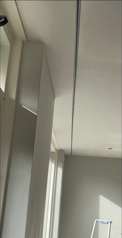 De ingestucte gordijnrails langs een gestucte wand en plafond